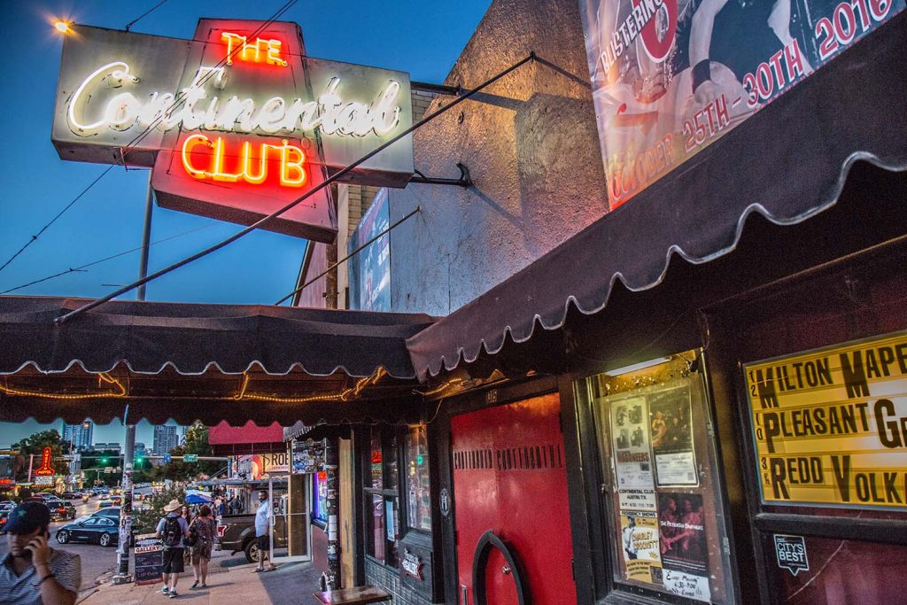 A diverse group of music enthusiasts dancing outside The Continental Club. The neon sign and front door of the Continental Club in Austin